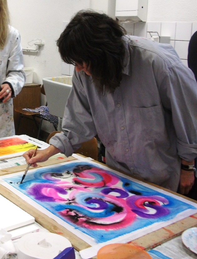 Während eines Kurses arbeitet Miriam Sacha konzentriert an einem abstrakten violett-blau gehaltenem Bild.